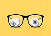 Large eyeballs behind eyeglasses on yellow background