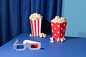 Cinema set-up with popcorn and 3D glasses against a blue background
