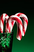 Red and white candy canes in a green glass on dark background