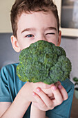 Young boy playfully covering his face with broccoli