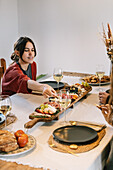 Woman serves food at cosy dinner party with friends