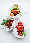 Freshly harvested tomatoes in eco-friendly bags on a light backg