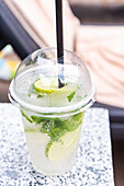 Refreshing lemonade with mint leaves in a clear plastic cup by the pool