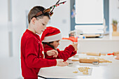Junge Zwillinge backen Plätzchen in einer weihnachtlich geschmückten Küche