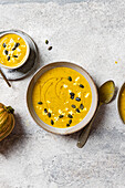 Creamy pumpkin soup with feta and seeds on grey background