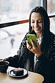 Stylish caucasian woman with braids using smartphone in a cafe