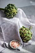 Two fresh artichokes styled with salt on a textured cloth