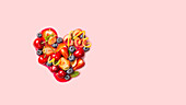 Healthy food arranged in the shape of a heart on a pink background