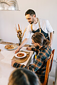 Private chef serves a man a gourmet meal at the dining table at home