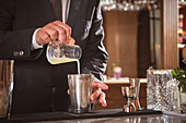 Barkeeper gießt in einem Nachtclub einen Cocktail aus einem Flachmann in einen Shaker