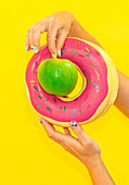 Green apple on a pink donut against a yellow background