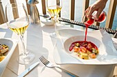 A person pouring sauce into a plate with a delicious seafood dish