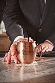 Barkeeper serviert Cocktail in Kupferbecher in Bar