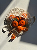 Top view of mandarins in a mesh bag on a sunny table
