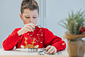 Boy in festive jumper bakes Christmas biscuits