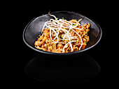 Gebratenes Nudelgericht in schwarzer Schüssel auf dunklem Hintergrund