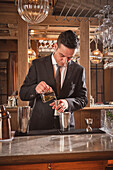 Bartender pouring alcohol into a measuring cup while preparing a cocktail
