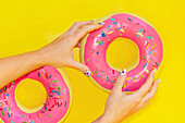 Vibrant Hands Holding a Pink Donut on Yellow Background