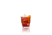 Classic Negroni cocktail with ice and an orange twist in a short glass on a reflective white surface