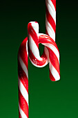 Close-up of intertwined candy canes on green background