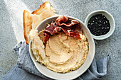 Top view of hummus with jamon and toast in a ceramic bowl