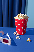 Cinema supplies with popcorn and 3D glasses on blue