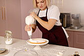 A woman carefully decorates a cake in the kitchen at home