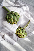 Two fresh artichokes on a textured white cloth in natural light