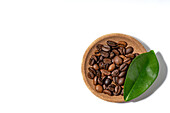 Coffee beans in a wooden bowl with a green leaf on white