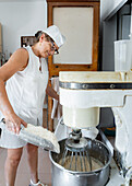 Woman mixing ingredients in an industrial mixer in a bakery kitchen
