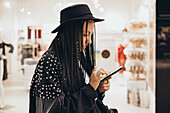 Fashionable woman with pigtails using her smartphone in a boutique