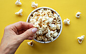A woman's hand takes popcorn from a cup