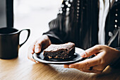 Close-up of hands holding a brownie and a coffee cup