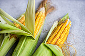 Close-up of fresh corn on the cob with husk on natural surface
