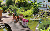 Mediterraner Garten mit Teich, Teichbrücke und üppigen Pflanzen im Sommer