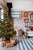 Weihnachtlich dekoriertes Wohnzimmer mit Backsteinwand und beleuchtetem Tannenbaum