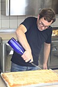 France, Gard, Petite Camargue, Aigues-Mortes, pastry baker Laurent Poitavin watering the Aigues-Mortes sugar fougasse with orange flower water