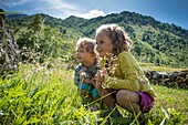 France, Savoie, Mountain of Vanoise, Pralognan la Vanoise, 2 young squatting children observe insects in alpine grasses