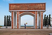 Benin, Ouidah, Frau, die als Zeichen der Freiheit Luftballons steigen lässt, unter der Tür ohne Wiederkehr, 1995 von der UNESCO errichtet, Symbol der Sklaverei