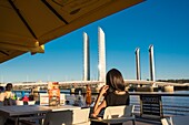 France, Gironde, Bordeaux, the Jacques Chaban Delmas lifting bridge spans the Garonne seen from a bistro terrace on the quays