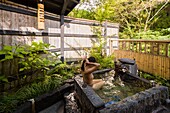 Japan, Kyushu island, Kumamoto region, Kurokawa Onsen, Ryokan Okunoyu, traditional luxury inn located in a spa town, young Asian woman bathing in the natural stone basin placed on the balcony of her room