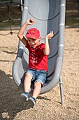 Boy with red hat and t-shirt playing on slide