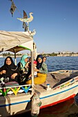 Egypt, Upper Egypt, Nile Valley, Luxor, Egyptian women smiling on a river shuttle crossing the Nile in front of the city of Luxor