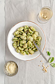 Portion Kartoffelgnocchi mit Basilikum-Pesto-Sauce auf hellgrauem Hintergrund.