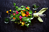 Cooking with herbs and edible flowers concept. Frypan skillet on dark background.