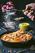 Side shot of a cast iron skillet with crimped phyllo, action with male hand holding a sifter of icing sugar