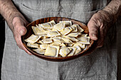 The skilful hands of a chef hold a wooden plate containing raw ravioli, fresh and expertly shaped, ready to be cooked