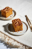 Pumpkin pie square with swirls of almond butter on a neutral background with golden forks
