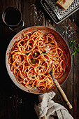Just prepared spaghetti in a pan, on a dark wooden table. View from above