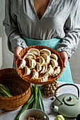 A cook holding a bamboo tray with uncooked gyoza dumplings,bamboo steamer,teapot,fresh green onions and mushrooms,Asian cuisine